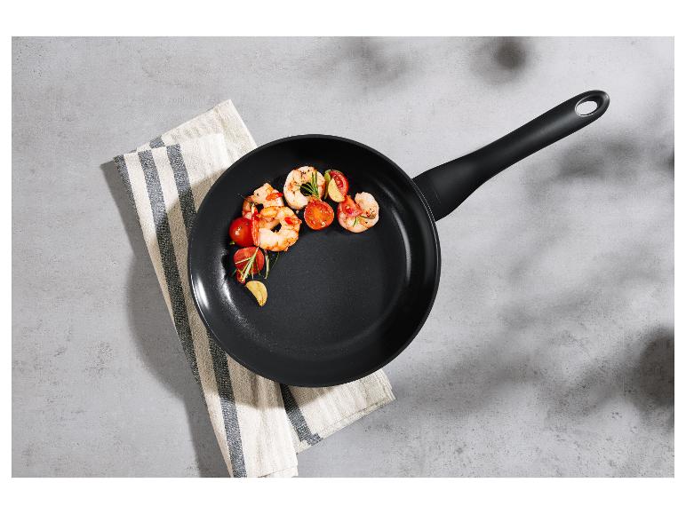Crevettes et tomates cerises dans une poêle noire sur un torchon rayé.