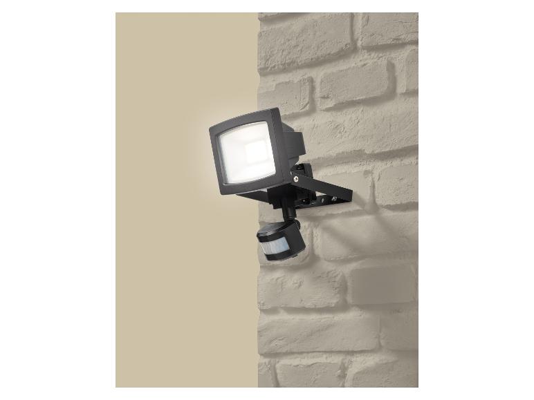 Projecteur extérieur avec détecteur de mouvement, monté sur un mur de briques.