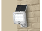 Lampe solaire LED argentée avec détecteur de mouvement, fixée sur un mur de briques beige.