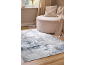 Tapis gris et blanc sur parquet avec pouf et coussin beiges.