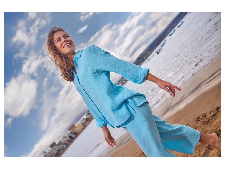 Femme en chemise et pantalon en lin bleu clair sur la plage, regardant vers le haut.