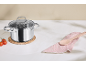 Casserole en acier inoxydable avec couvercle en verre, cuillère en bois sur serviette rose et tomates.