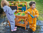 Deux enfants jouent avec des vêtements de pluie dans le jardin, près d'une cuisine en bois pour enfants.