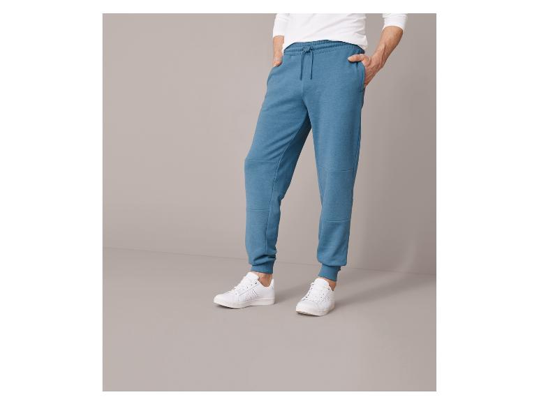 Un homme portant un pantalon de survêtement bleu et des baskets blanches.