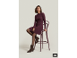 Femme en robe en maille violette, collants et bottines marrons, assise sur un tabouret haut