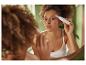 Une femme utilise un épilateur Braun pour ses sourcils devant un miroir.