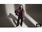 Une femme en doudoune violette, pull noir et pantalon noir posant dans un studio.