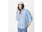 Femme en chemise rayée bleu clair, jean et casquette beige.