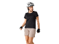 Femme en casque de vélo blanc, t-shirt noir et short beige, avec des gants de cyclisme.