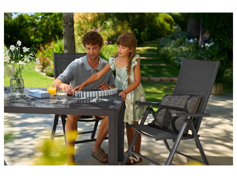 Père et fille jouant aux dominos à une table de jardin avec des chaises en extérieur.