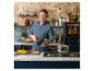 Jamie Oliver dans une cuisine rustique, tenant une poêle, avec des légumes sur le comptoir.