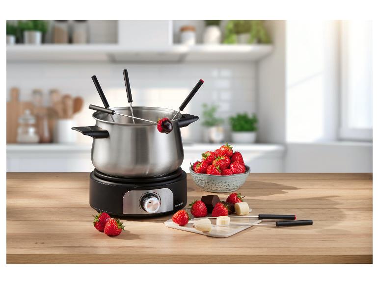 Service à fondue électrique avec fraises, chocolat et bananes sur une table en bois.