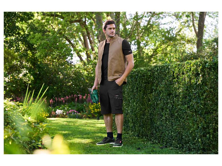 Homme en gilet de jardinage et short Parkside taillant une haie.