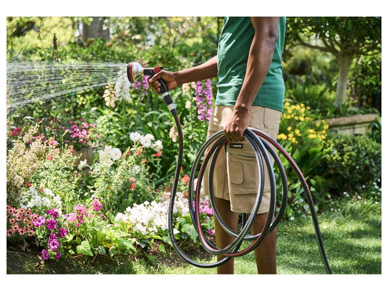 Personne arrosant un jardin luxuriant avec un tuyau et un pistolet, tenant le tuyau enroulé.