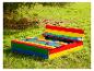Bac à sable en bois coloré avec bancs, dans un jardin vert sous un arbre.