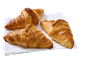 Trois croissants dorés et fraîchement cuits sur une serviette blanche.