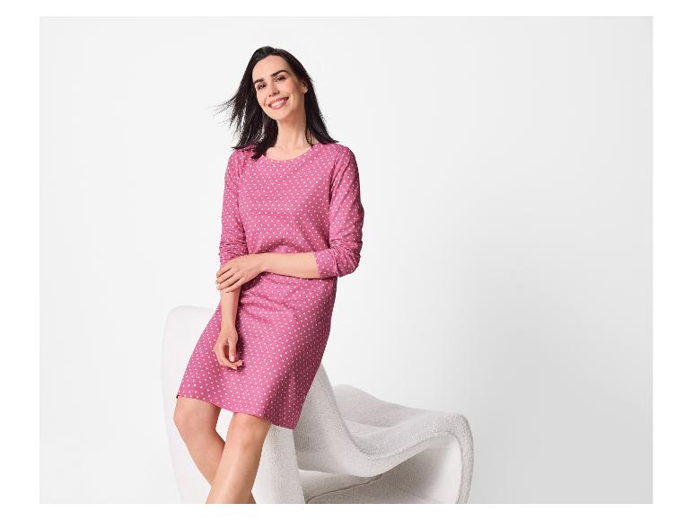 Femme en robe rose à pois assise sur une chaise blanche, souriante.