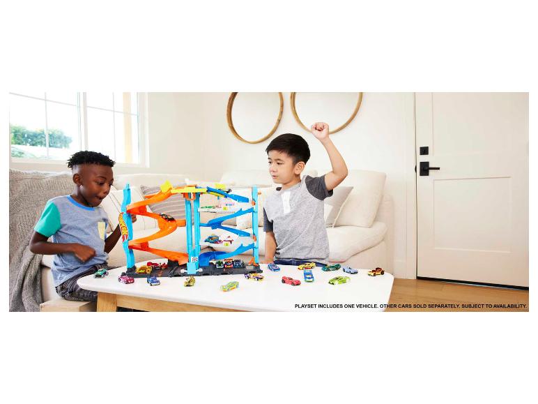 Deux enfants jouent avec un ensemble de garage Hot Wheels et plusieurs petites voitures.