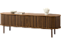 Buffet ovale en bois avec portes à lattes, un bol décoratif, un livre et un vase dessus.