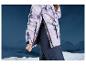 Femme portant une veste de ski à motif marbré et un pantalon de ski devant des montagnes.