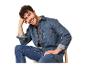 Homme souriant en chemise et jean en denim, assis sur une chaise.