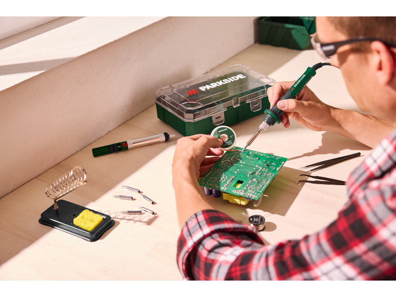 Homme soudant une carte de circuit imprimé avec un fer à souder, de la soudure et des outils.