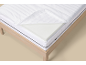 Matelas avec housse ouverte et couche de mousse, sur un cadre de lit en bois.