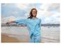 Femme en chemise et pantalon bleu clair sur une plage avec une ville en arrière-plan