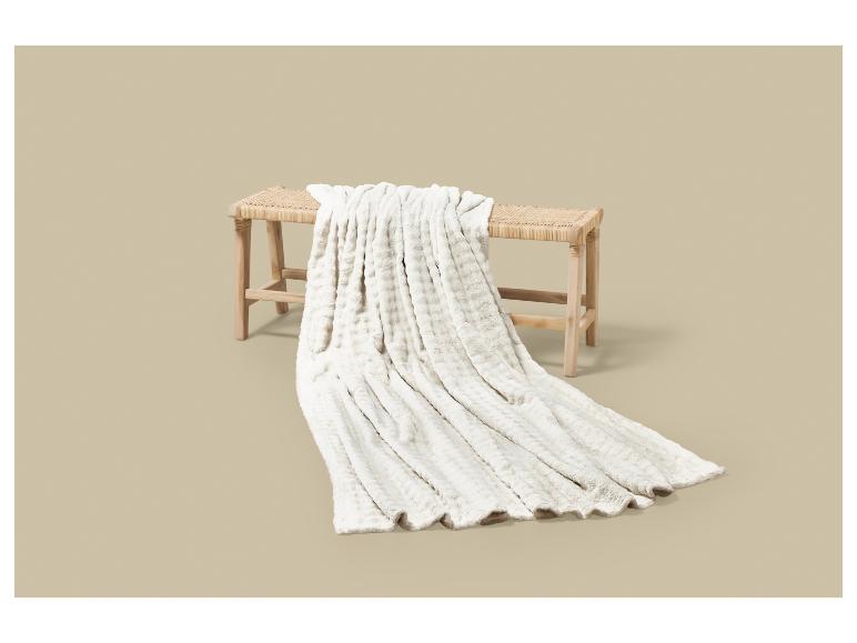 Plaid blanc doux sur un banc en bois avec assise en rotin.