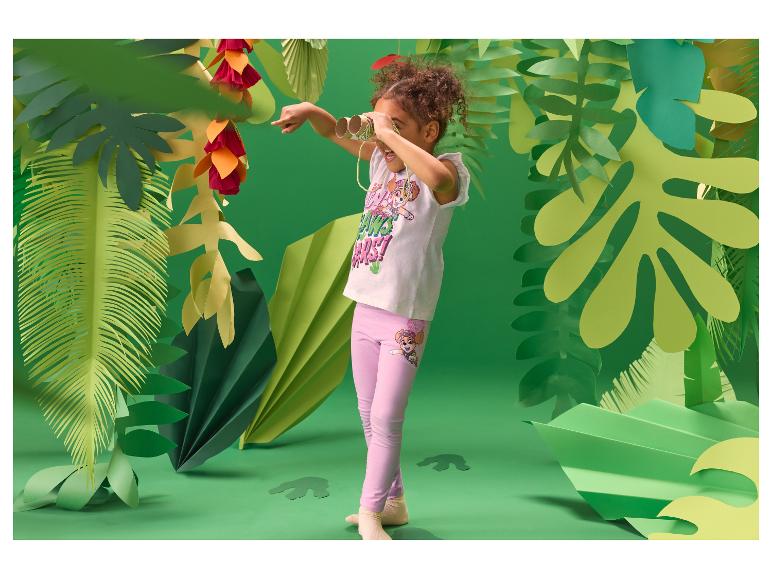 Fille dans un décor de jungle, portant un t-shirt blanc et un legging rose, regardant à travers des jumelles.