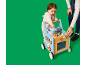 Bébé joue avec une cuisine jouet en bois et un trotteur, assisté par un adulte.