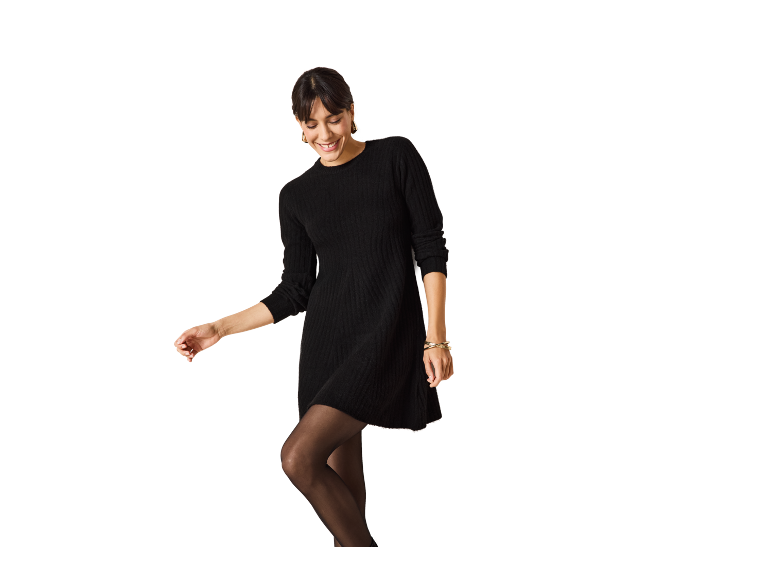 Femme souriante en robe en maille noire et collants posant sur fond noir