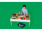 Enfant jouant avec une table de jeu en bois avec train et accessoires.