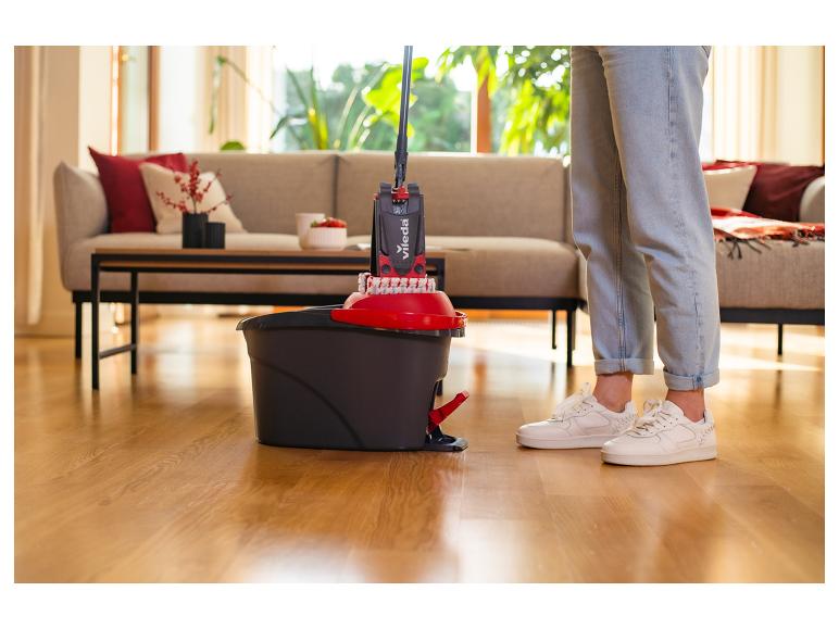 Personne utilisant une serpillière et un seau Vileda pour nettoyer un parquet dans un salon.