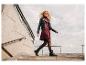 Femme en robe bordeaux, veste en cuir noire et bottes noires descendant des escaliers extérieurs.