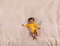 Un bébé en combinaison jaune allongé sur une couverture rose avec un hochet.