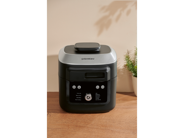 Multicuiseur noir et argenté avec diverses fonctions de cuisson sur une surface en bois.
