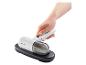 Aspirateur à main blanc avec bac à poussière transparent, en charge sur une base noire.