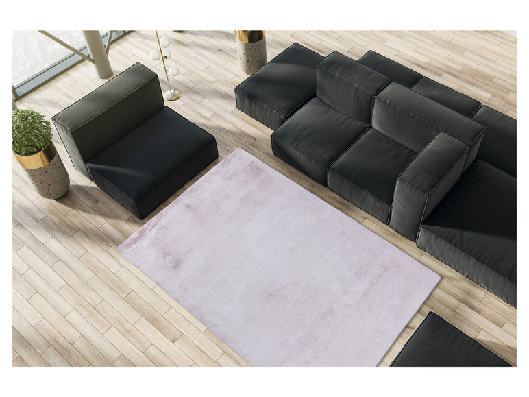 Un tapis rose sur un sol en bois avec un canapé modulaire noir.