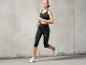 Une femme portant un soutien-gorge de sport noir, un legging et des baskets blanches en courant.
