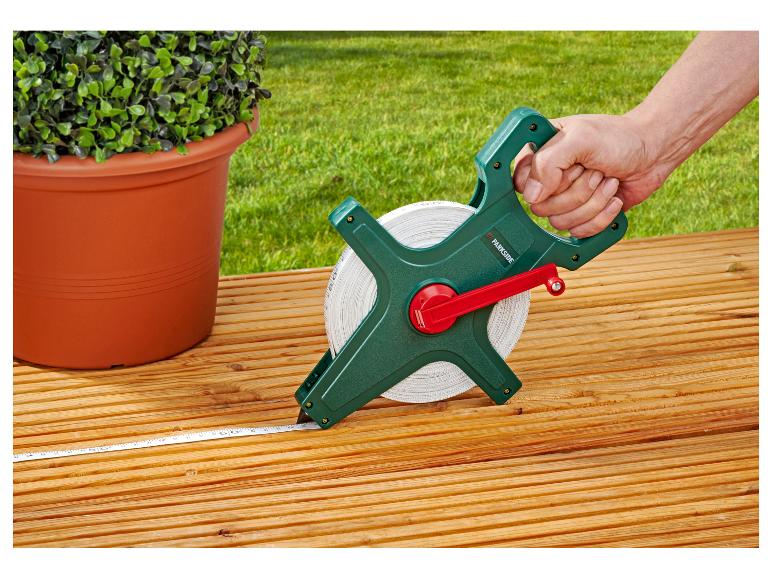 Main tenant un mètre ruban sur une terrasse en bois à côté d'une plante en pot.