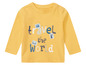 Un t-shirt jaune à manches longues avec le texte 'Travel the World' et des images de timbres-poste.