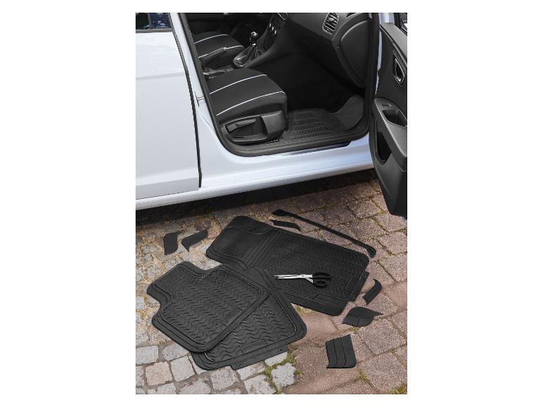 Tapis de sol de voiture et pièces découpables avec des ciseaux à côté d'une portière de voiture ouverte.