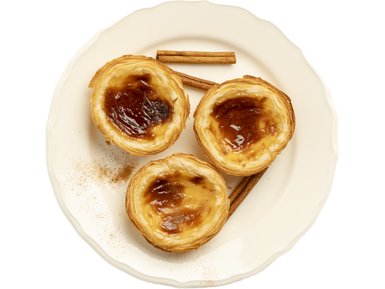 Trois tartelettes crémeuses Pastel de Nata à la cannelle sur une assiette blanche.