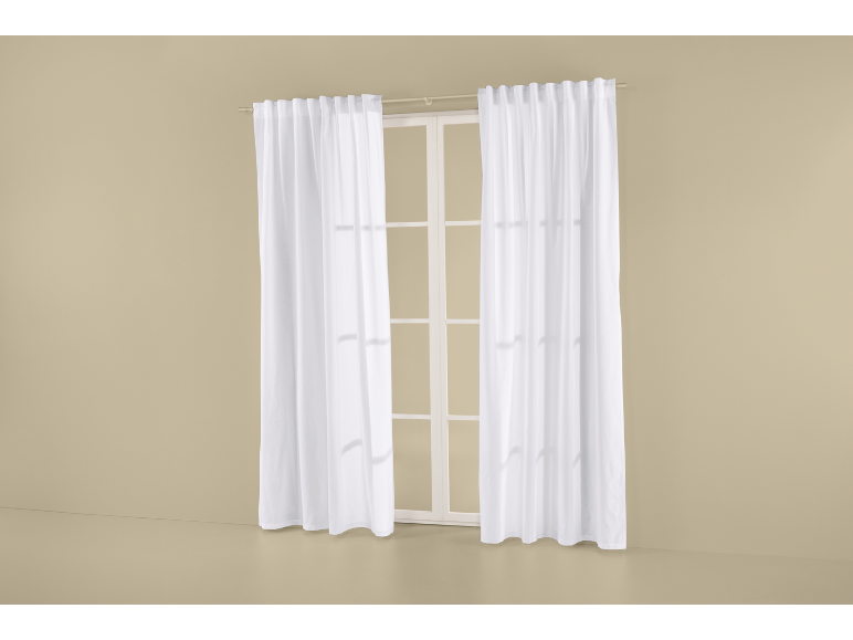 Rideaux blancs translucides suspendus à une fenêtre à cadres blancs sur un mur beige.