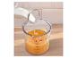 Du lait est versé dans un verre doseur transparent avec du jus d'orange sur une surface en bois.