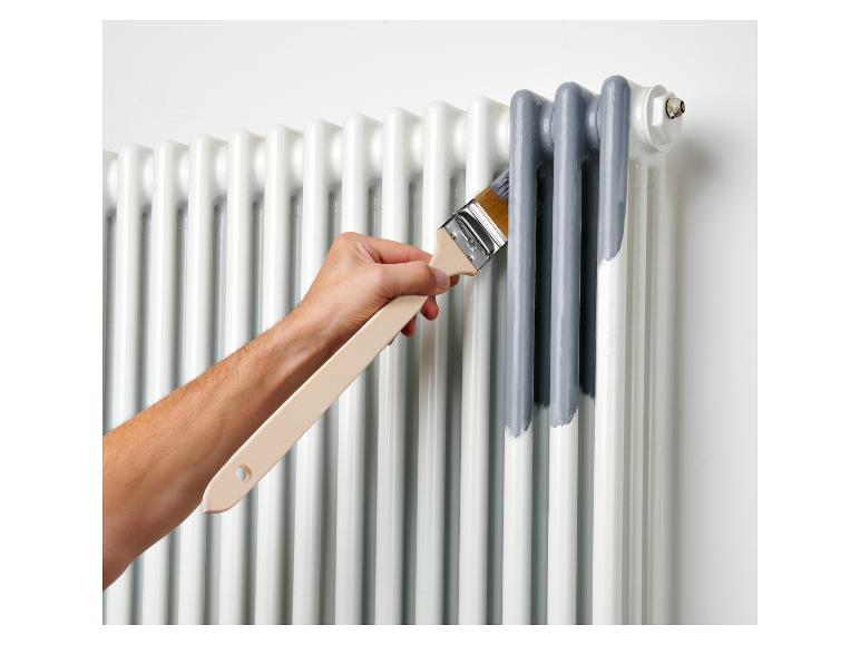 Main peignant un radiateur blanc avec de la peinture grise