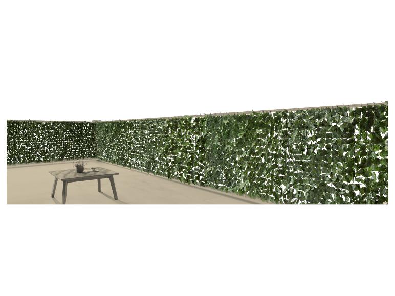 Clôture de feuilles artificielles avec table d'extérieur et vase sur une terrasse.
