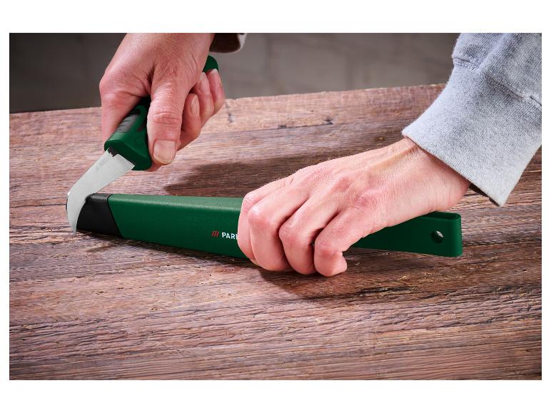 Mains insérant une lame courbée dans un étui vert sur une table en bois.
