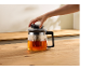 Main posant un couvercle sur une théière en verre avec du thé sur une table en bois.